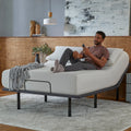 Lifestyle image of a man sitting on a Baselogic adjustable base using the wireless remote to find the perfect sleeping position.
