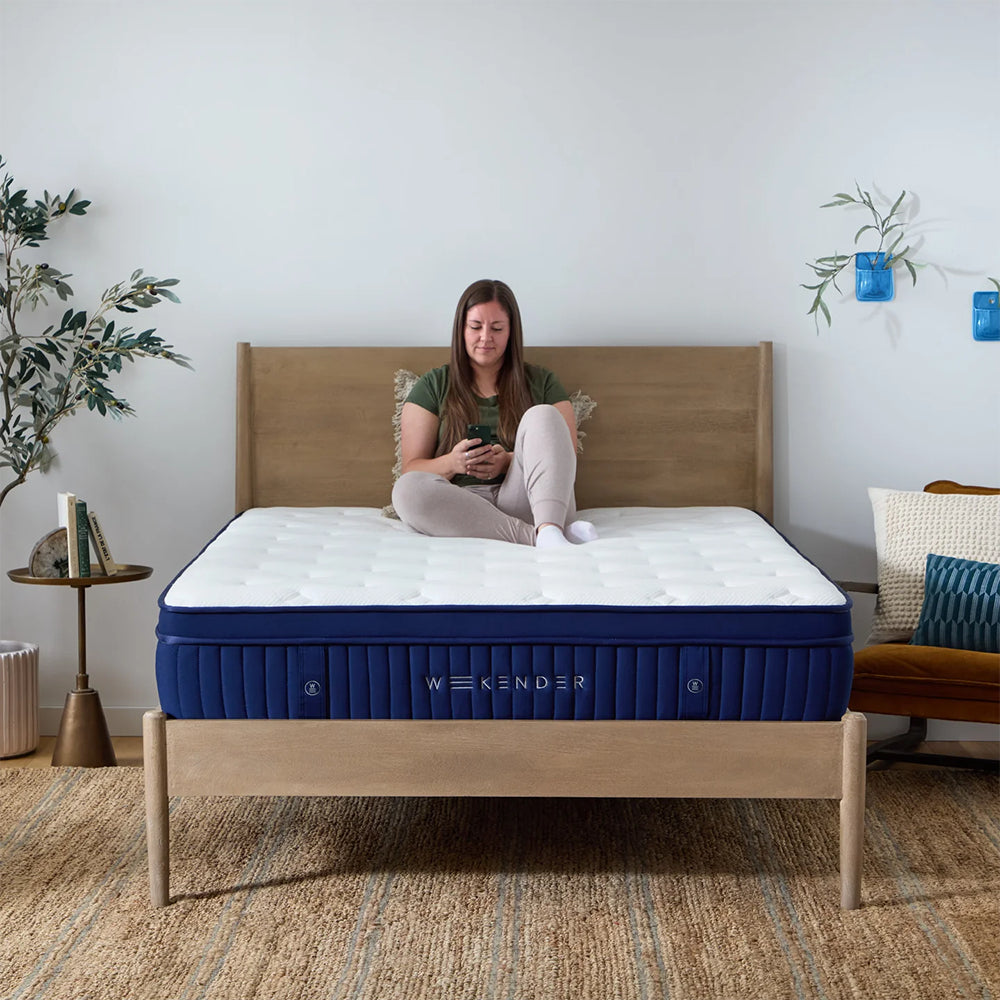 Lifestyle shot of a woman relaxing on the center of the Weekender 13-inch Euro top hybrid mattress in a sunlit master bedroom.

