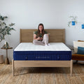 Lifestyle shot of a woman relaxing on the center of the Weekender 13-inch Euro top hybrid mattress in a sunlit master bedroom.
