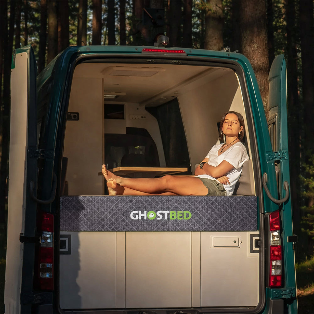 Woman lounging on a GhostBed RV 10-inch hybrid mattress inside a camper van, showcasing van life comfort and style.
