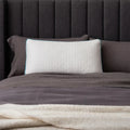 Malouf FlexFill hybrid pillow with HyperChill cooling cover styled on a dark gray upholstered bed frame.
