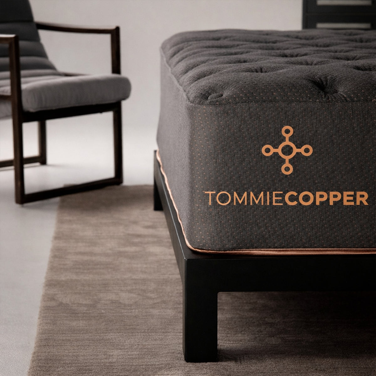 Close-up of the embroidered Tommie Copper brand logo on the charcoal fabric side panel of a 14-inch luxury firm hybrid mattress.
