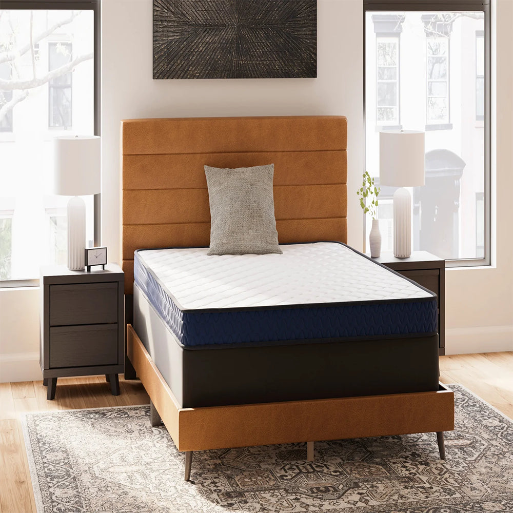 Firm 6-inch Mattress by Ashley styled on a tan upholstered platform bed in a modern urban master bedroom setting.
