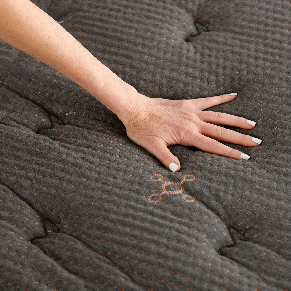 Hand pressure test on the quilted top of a Tommie Copper Core Znergy mattress highlighting the pressure-relieving memory foam and copper-infused fabric.
