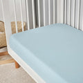 Light blue Hyper-Linen performance crib sheet on a white wooden crib for a cool, dry sleep environment.
