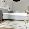 Low-profile side view of the EcoCore Hybrid Deluxe mattress on a grey tufted bed frame, illustrating its 12-inch depth and supportive layers.
