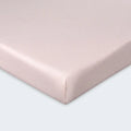 Detailed corner view of a pink moisture-wicking Hyper-Wool fitted crib sheet for a snug mattress fit.
