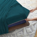 Hands applying a teal Hyper-Cotton fitted sheet with Powerband to stay secure on the mattress.
