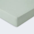 Close-up of a sage green moisture-wicking performance crib sheet corner for standard nursery mattresses.
